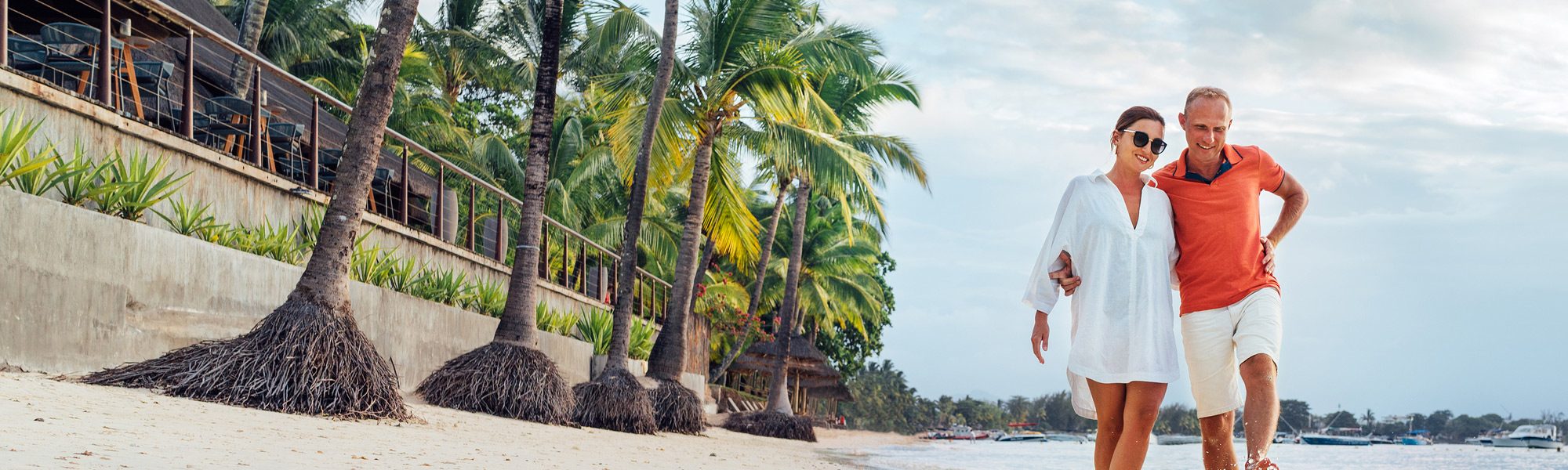 Couple kicking the water as they walk along a beach restaurant